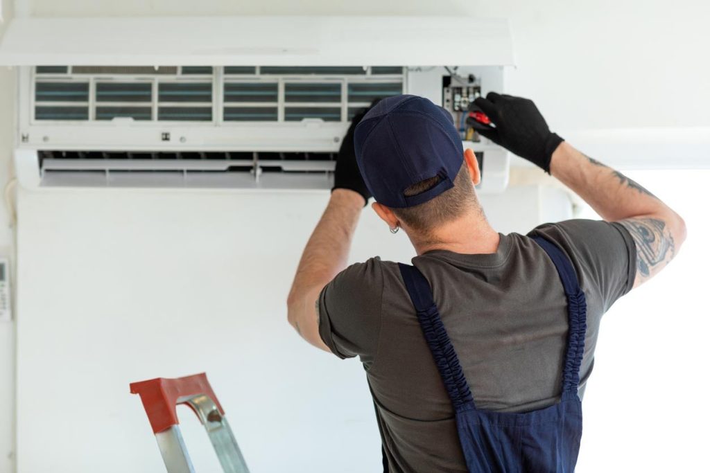 A technician is repairing an air conditioner on a wall.