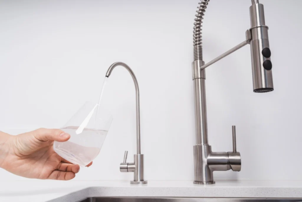 Hand holding a glass under a sleek modern kitchen faucet with water flowing.